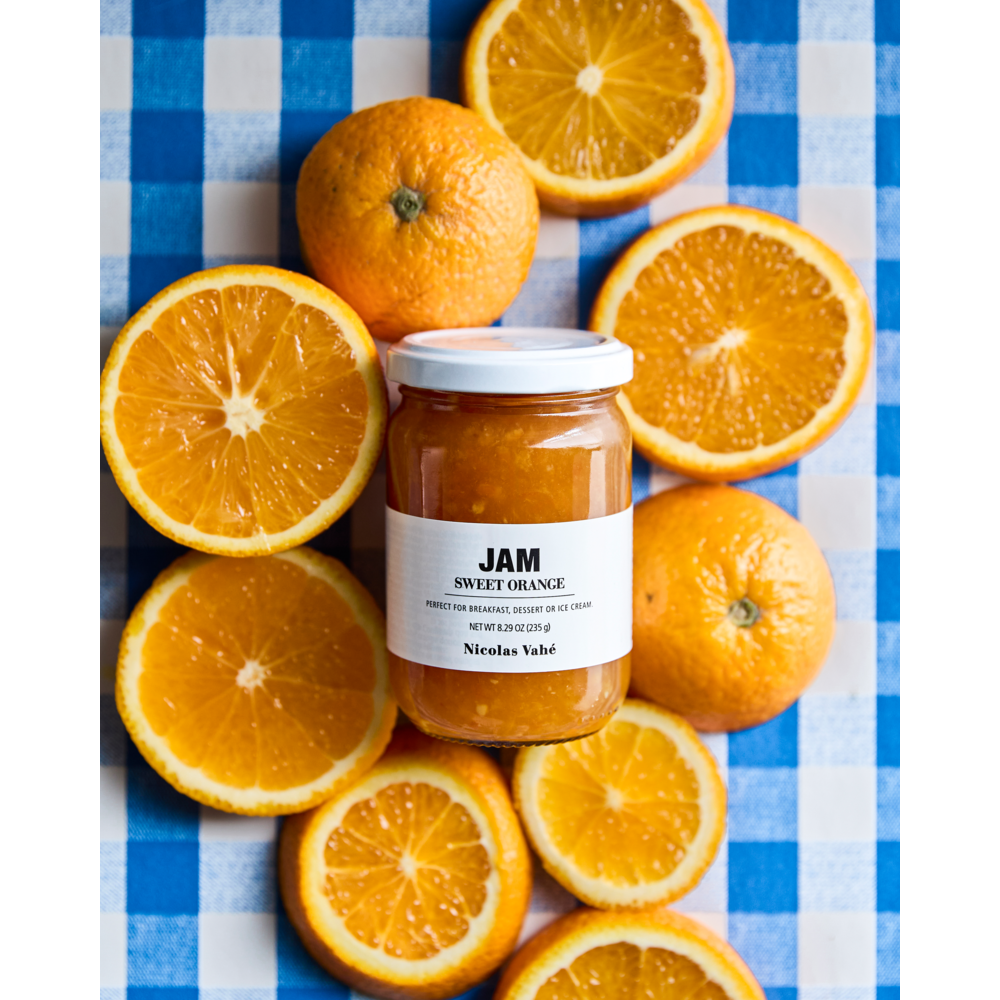 A jar of Nicolas Vahé Jam Seasonal, Sweet Orange surrounded by orange slices on a blue and white checkered surface.