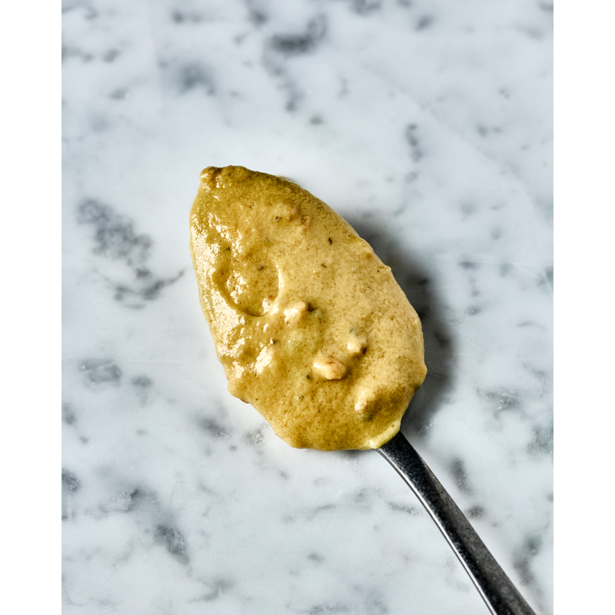 A spoonful of Nicolas Vahé Mustard, Hazelnut & Truffle rests on marble, highlighting a festive condiment ideal for special occasions.