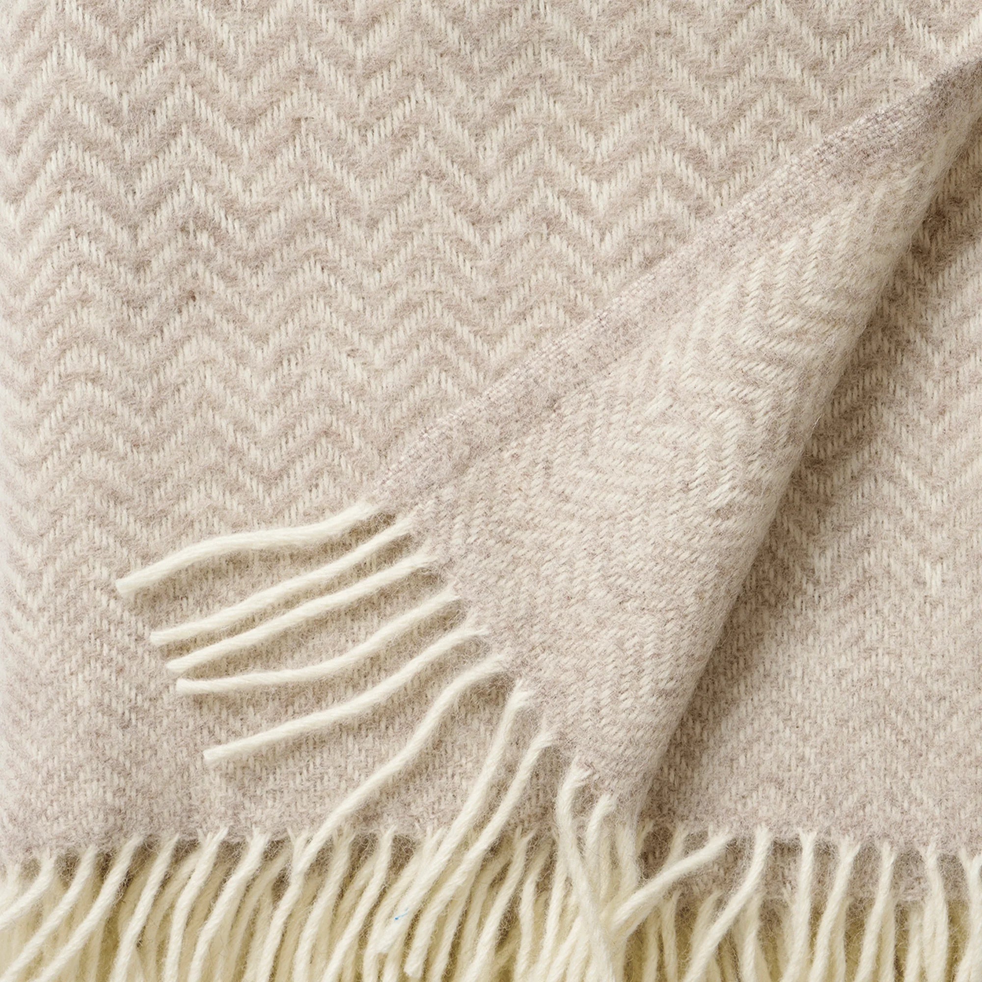 A close-up of Klippan’s Zigzag Throw in Lambswool, Greige, featuring a herringbone pattern and fringe with both sides and a folded corner—ideal for cozy, stylish home decor.