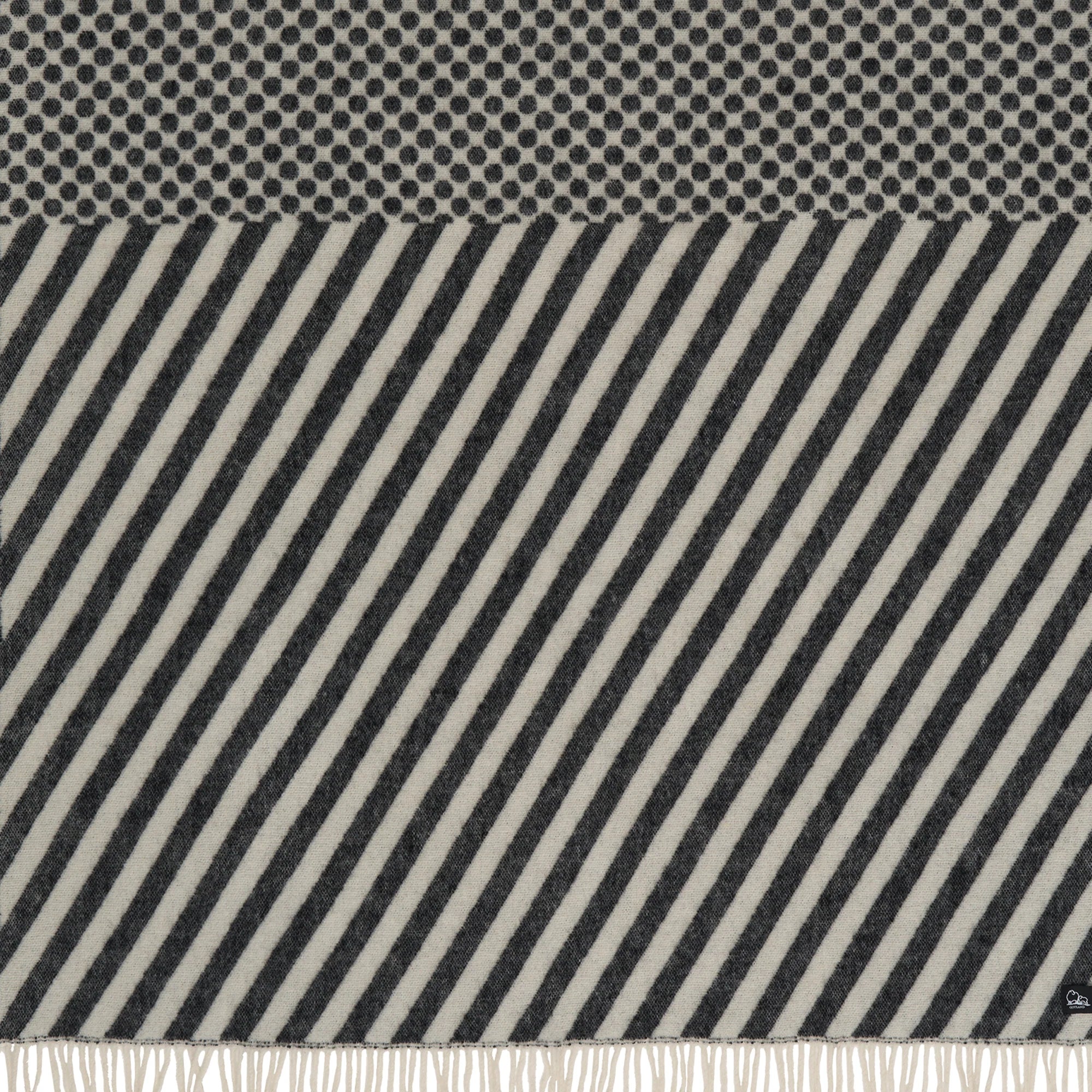 The Klippan Dot & Stripe Lambswool Throw in Black/White is perfect for home decor, featuring black and white polka dots on top, diagonal stripes below, and a white fringe at the bottom.