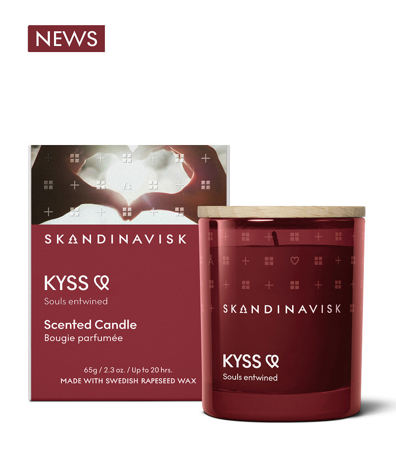 A Skandinavisk Scented Candle Kyss, 65g, with an engraved beechwood lid, is shown before its matching box featuring Nordic patterns and text describing the fragrance and ingredients.