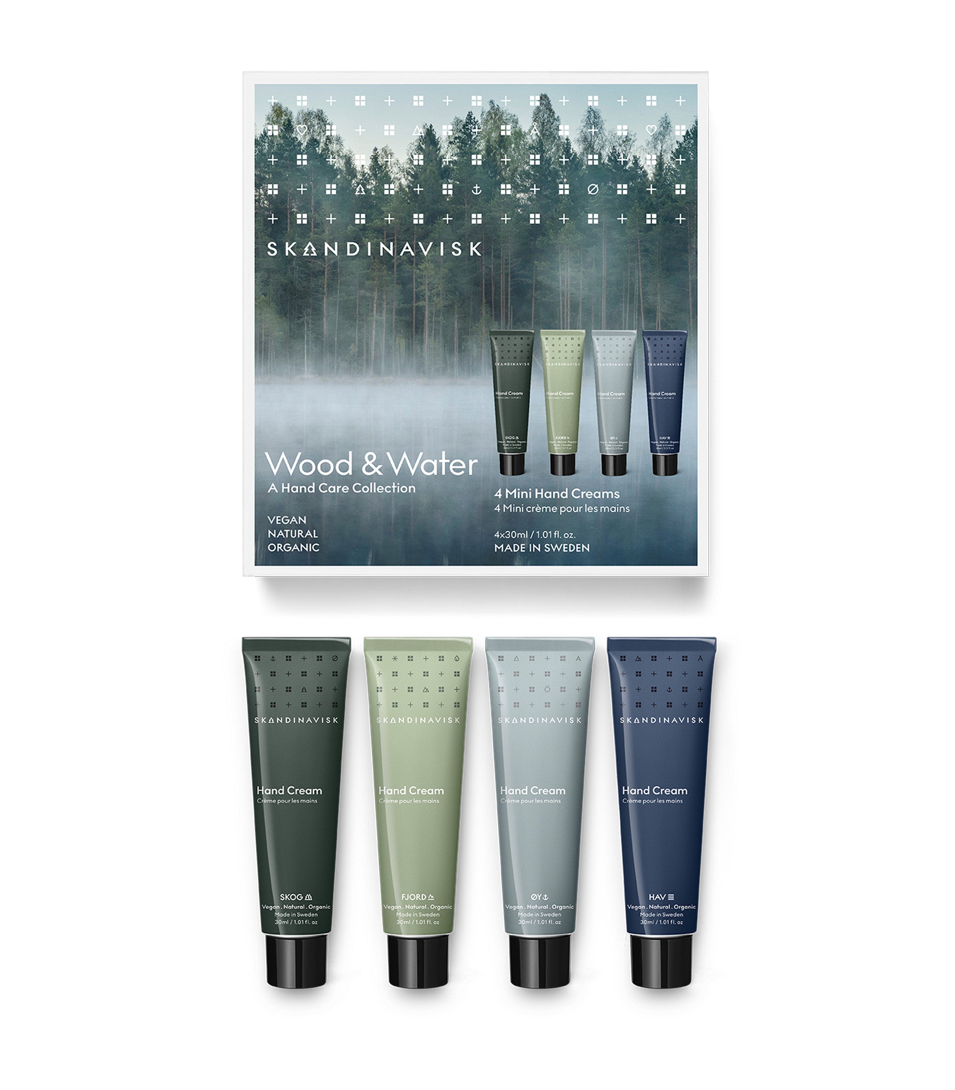 Four mini hand cream tubes in green, beige, blue, and gray—Skog, Fjord, Oy & Hav—are displayed below the Skandinavisk Giftset Hand Creams Wood & Water box, which features a misty forest background. Made in Sweden with natural ingredients, this organic and vegan hand cream set from Skandinavisk is beautifully packaged.