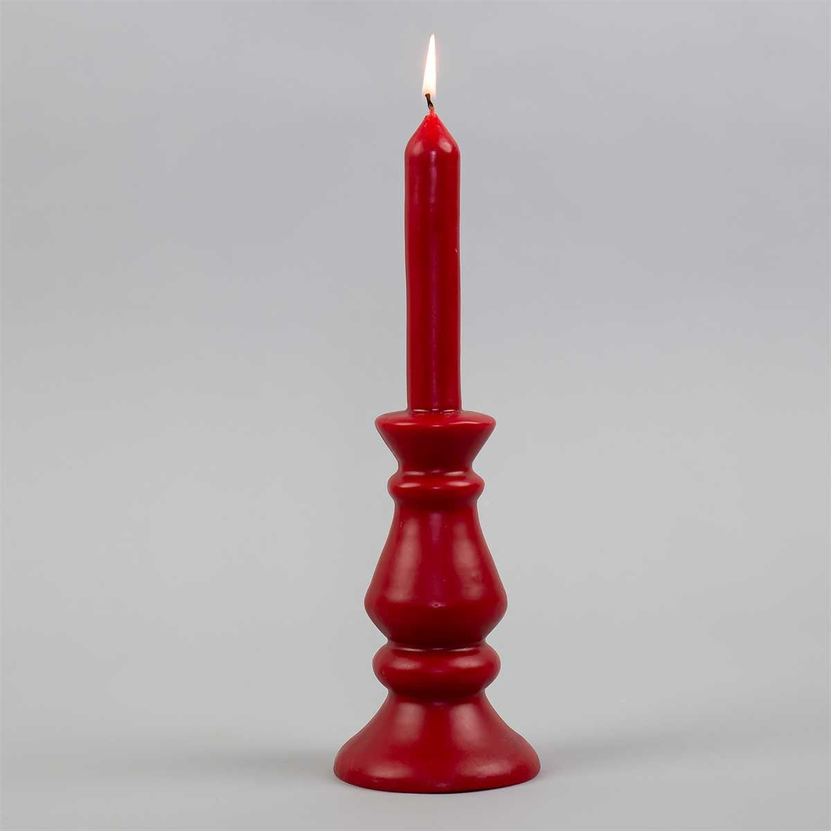 A lit Glow Candle, Red, in a matching handcrafted, sculpted red taper base.