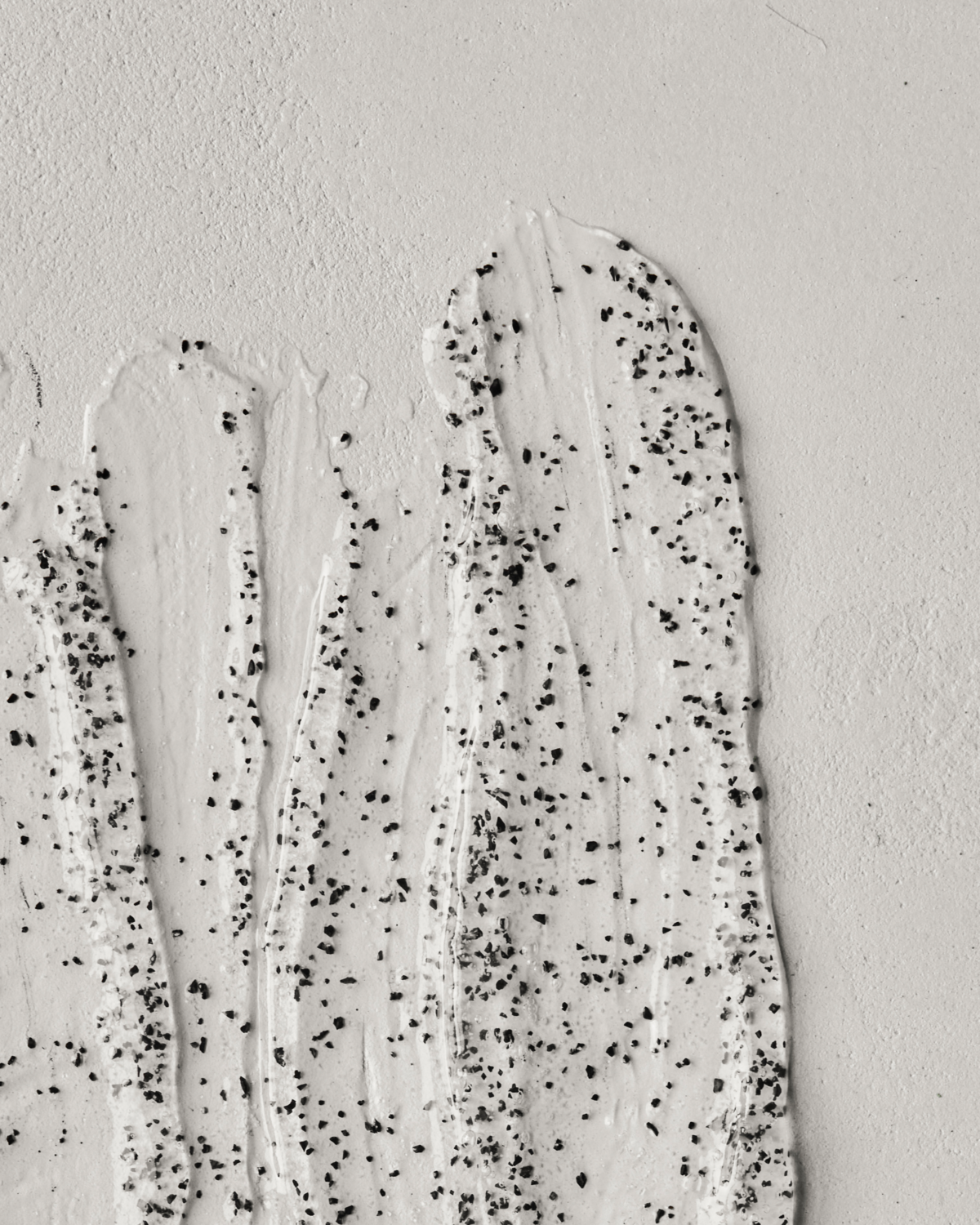 Close-up of Meraki’s Deep Valley Body Scrub (200 ml): a thick, white creamy formula with black exfoliating specks, spread in vertical streaks on a light surface—ideal for deep-cleansing exfoliation.