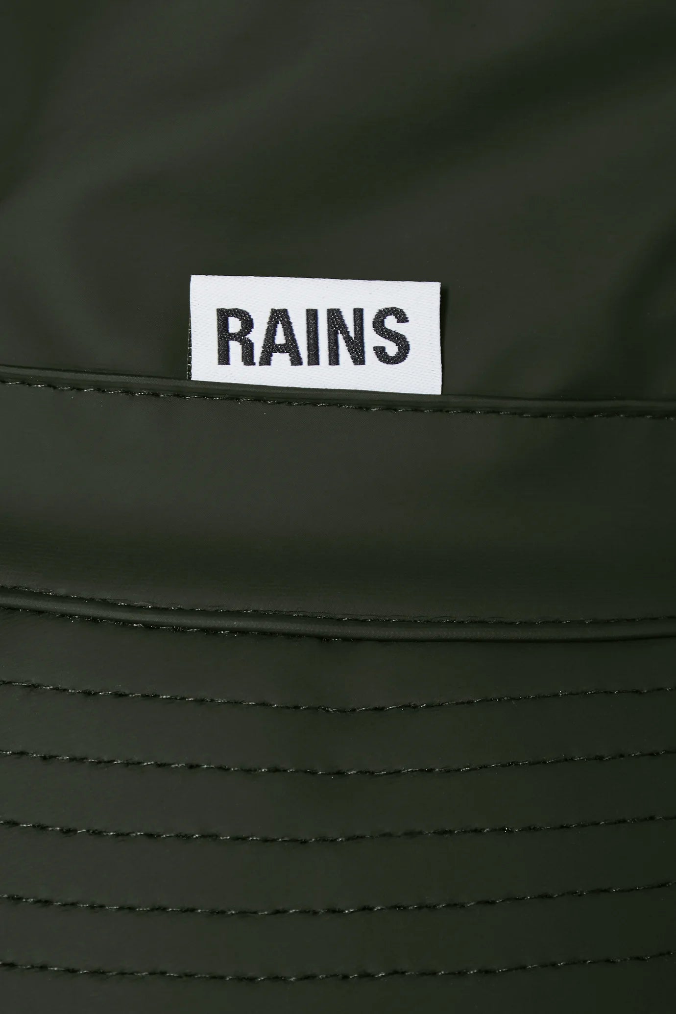 Close-up of the Rains Bucket Hat in Green shows waterproof PU fabric with a white RAINS label and visible stitching, highlighting its stylish design.