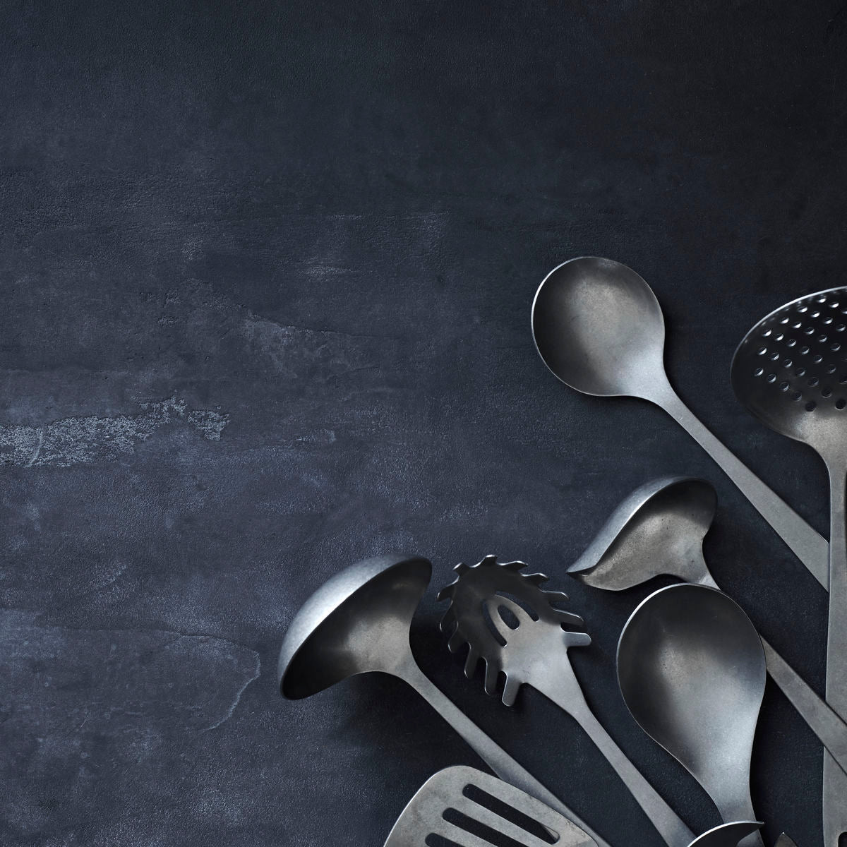 The Nicolas Vahé Sauce Spoon, Daily, with a silver finish, is displayed on a dark textured surface.