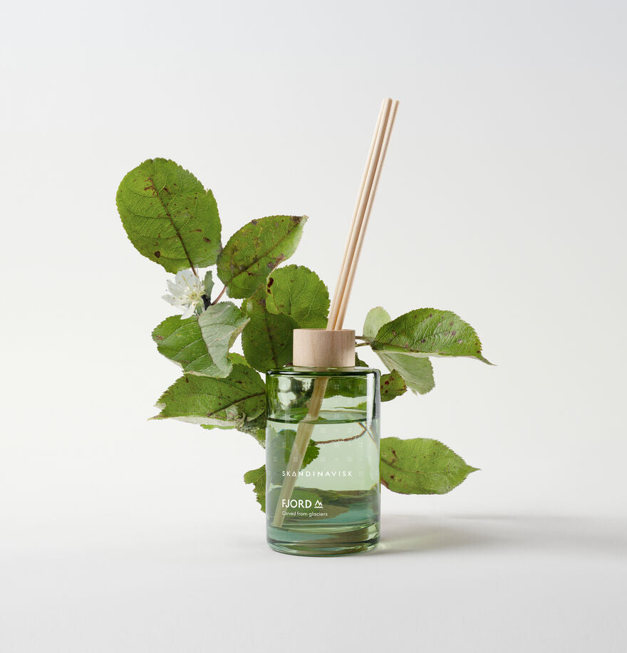 The Skandinavisk Scent Diffuser Fjord 200ml features a wooden cap, reed sticks, and green leafy branches for a fresh vegan room fragrance, shown on a plain white background.