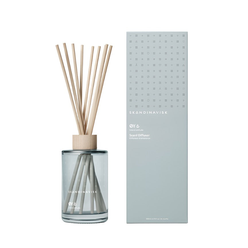 The Skandinavisk Scent Diffuser Øy, 200ml, features a glass vessel with light wooden sticks and sits beside its tall, light gray branded box—offering a vegan room fragrance for your space.