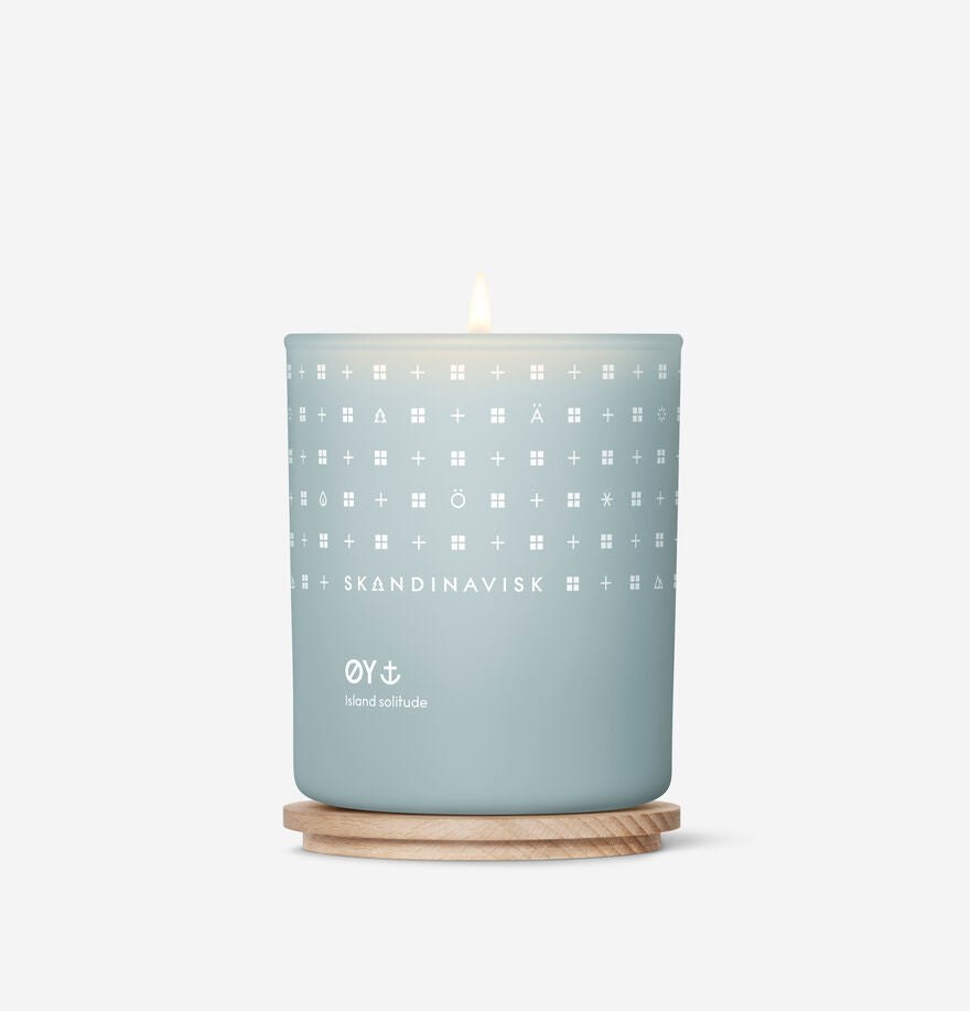 A lit Skandinavisk Scented Candle Oy 50h, 200g, crafted from Swedish rapeseed wax, sits on a round wooden base against a plain white background.