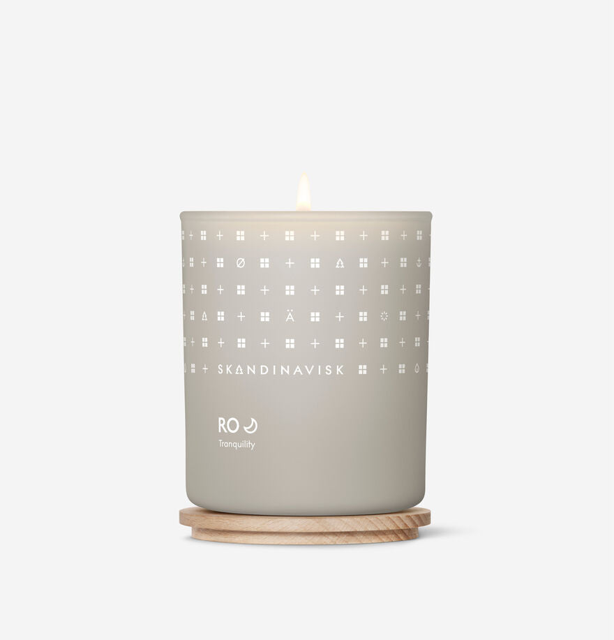The Skandinavisk Scented Candle Ro 50h, 200g sits in a light gray jar on a round wooden base, set against a white background. Made with Swedish rapeseed wax, this sustainable candle brings calm to any space.