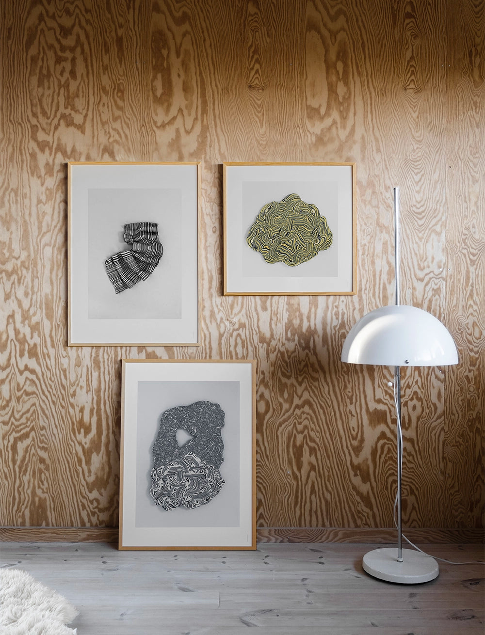 The Vibrant Print (50 cm x 50 cm) by Fine Little Day adds poetic energy to a wood-paneled wall, with a ceramic sculpture, white dome-shade floor lamp, and small white rug completing the light wood-floor setting.