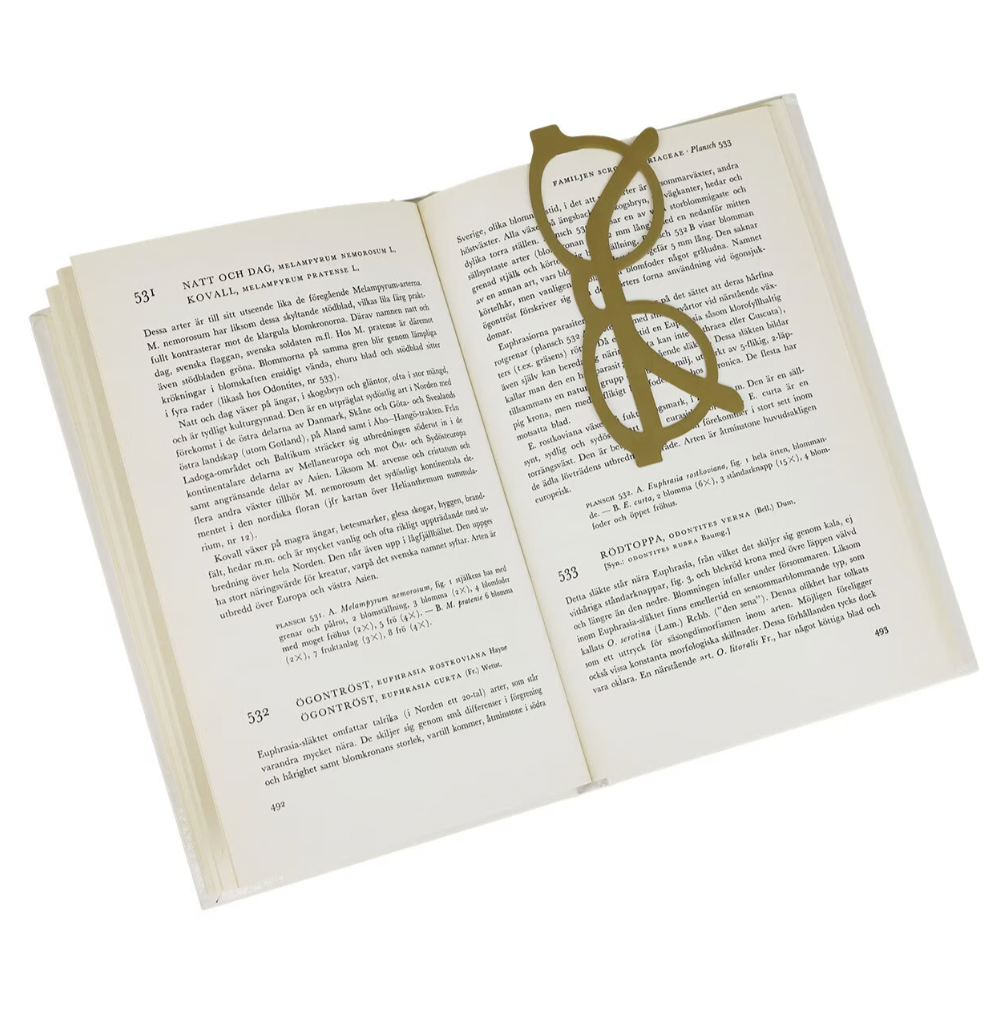 An open book with a Strömshaga Brass Book Marker, shaped like gold-colored glasses, resting on its pages.
