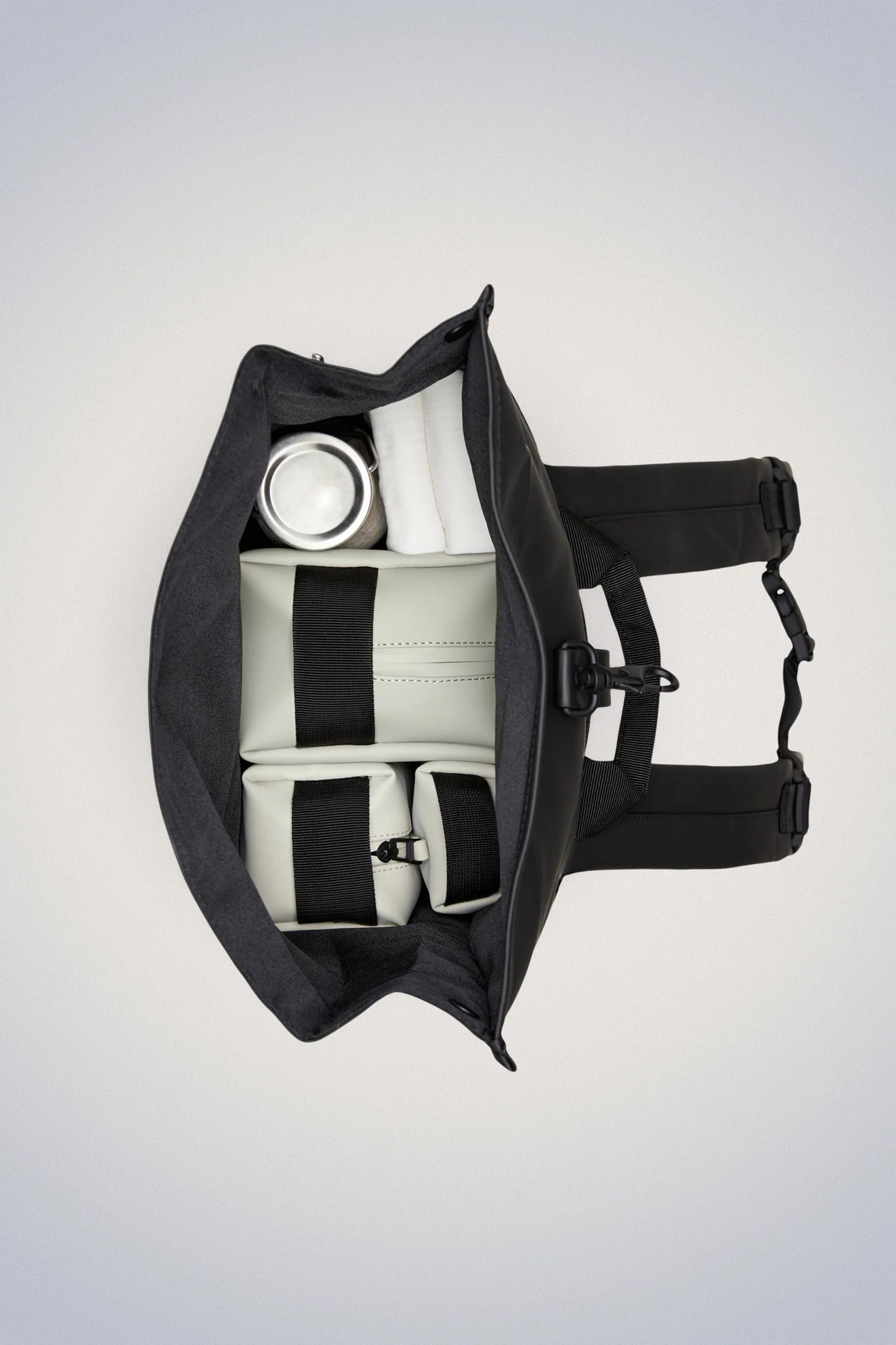 Top-down view of an open Rains Rolltop Rucksack Backpack in Green with organized compartments, including a laptop pocket, holding a white water bottle and several light-colored rectangular pouches.
