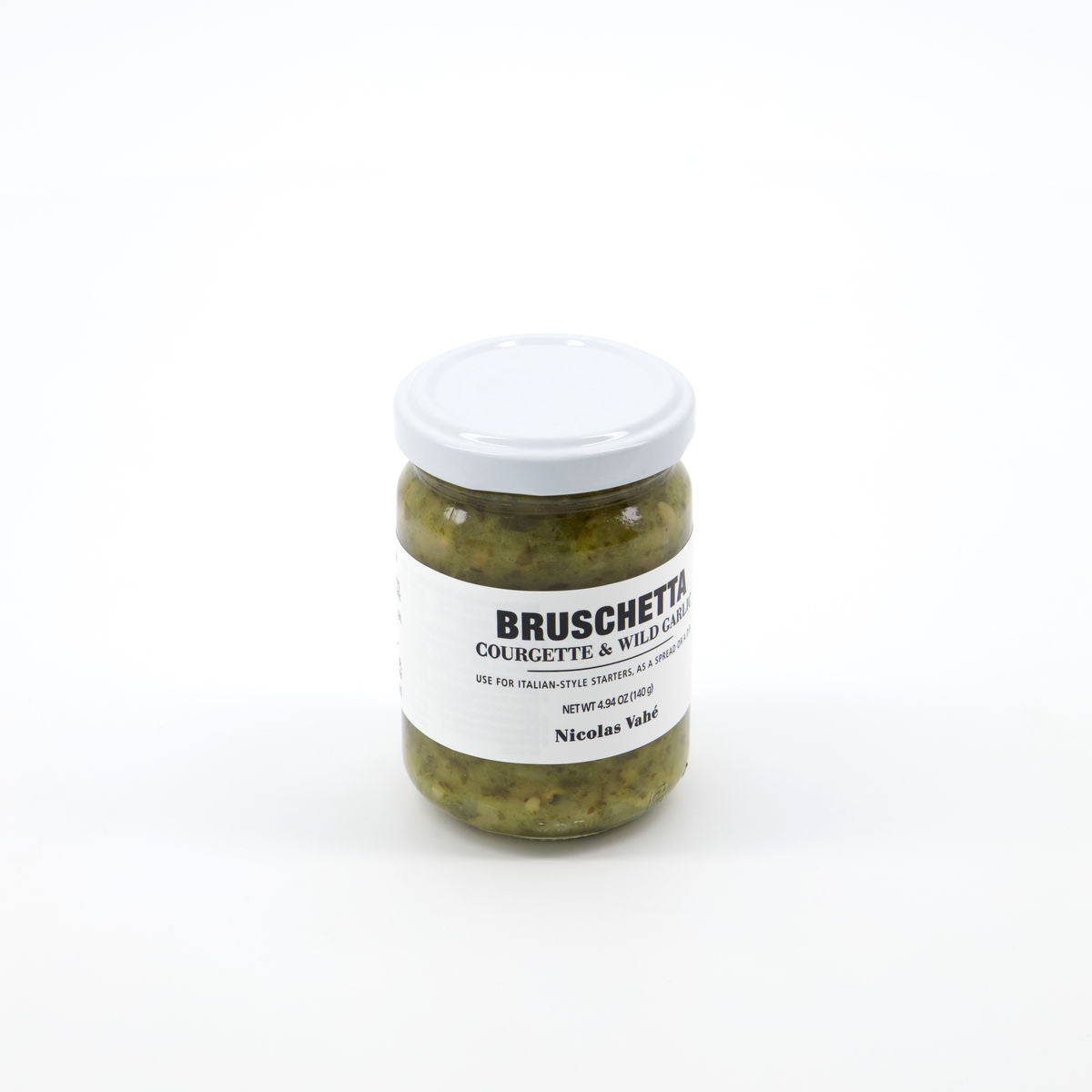 A glass jar of Nicolas Vahé Bruschetta, Courgette & Wild Garlic with a white lid sits on a plain white background. The label, in black and blue text, emphasizes the fresh flavors of courgette and wild garlic.