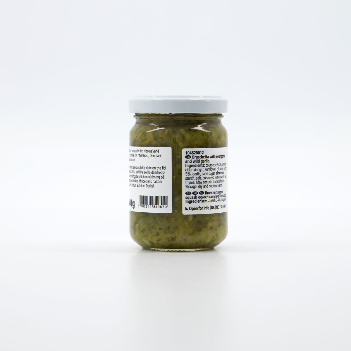 A small glass jar of Nicolas Vahé Bruschetta, Courgette & Wild Garlic, with a white lid and green chunky paste inside. The back label shows ingredients and product info. Perfect for bruschetta. Plain white background.
