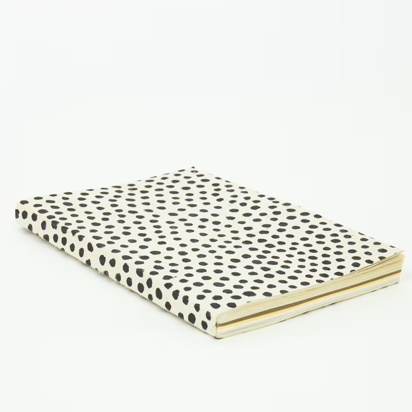 A World of Crafts Dotted Notebook, White, A5, featuring a handmade cover with black polka dots, rests closed on a white surface and is viewed from an angle.