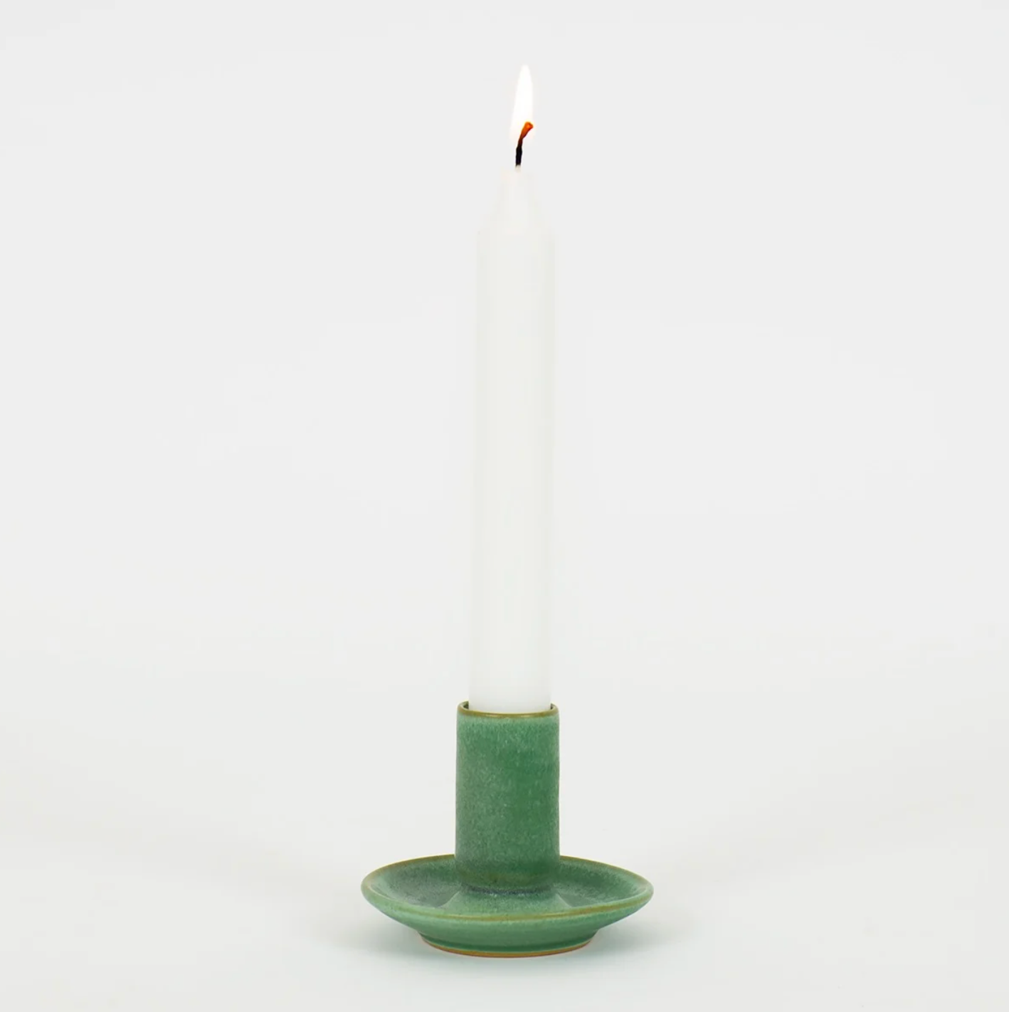 A white candle is placed upright in the green Hera Handmade Candle Holder by A World of Craft, featuring a saucer base, against a plain white background.