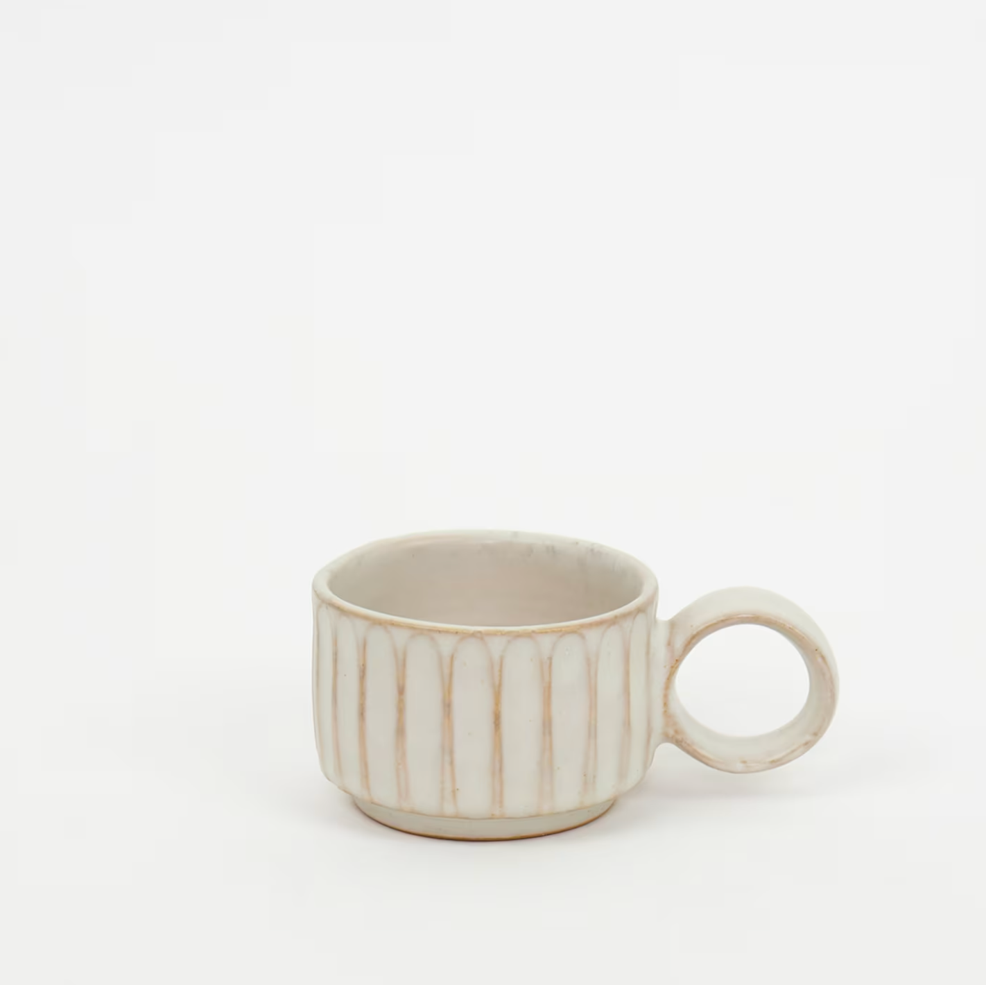 The Mini Rhea Handmade Cup by A World of Craft is crafted from stoneware clay in beige, featuring vertical ridges and a large round handle, shown on a plain white background.