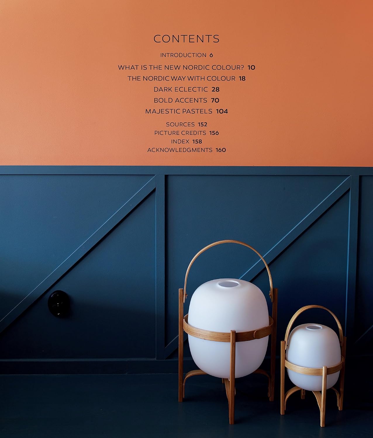 Two sleek white lamps with wooden frames rest on a dark blue floor, illuminating bold blue and orange walls—an ideal scene from Nordic Homes in Colour - The New Scandi Style by Antonia af Petersen for fresh interior inspiration.