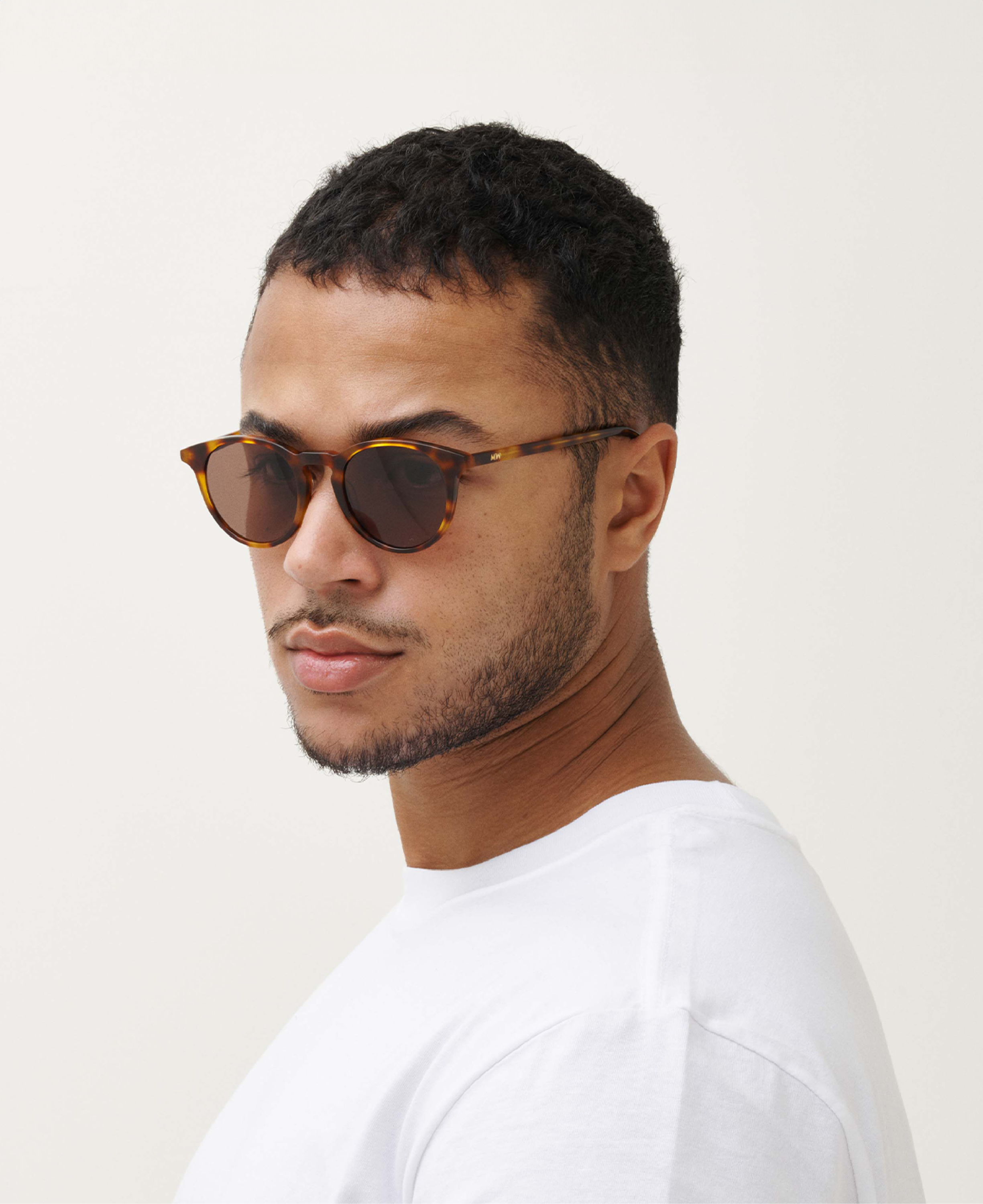 Man with short hair wears MESSYWEEKEND Sunglasses New Depp in Tortoise Brown with brown lenses and acetate frames, styled with a white t-shirt, facing sideways and looking toward the camera against a plain background.