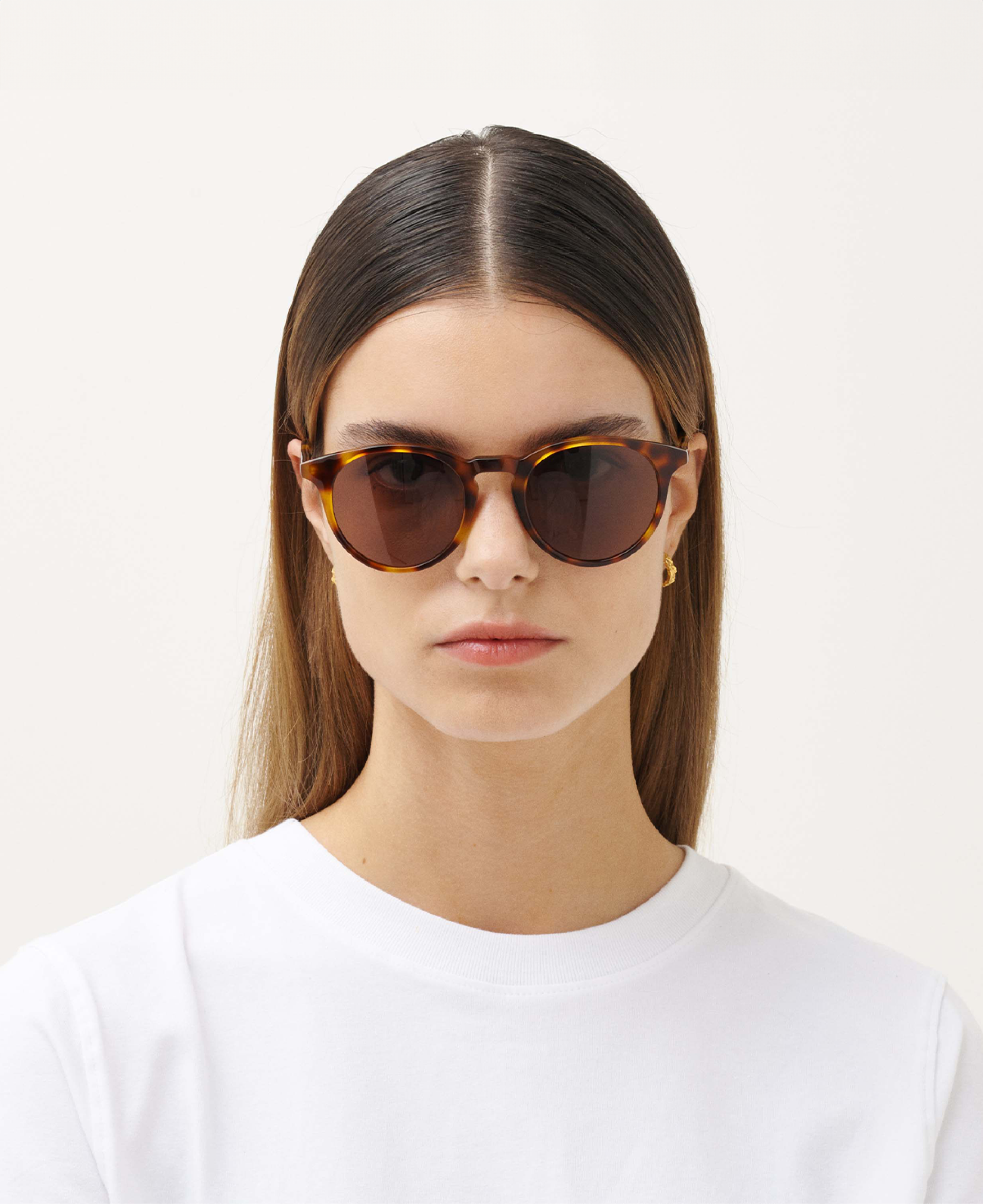 A woman with straight brown hair wears MESSYWEEKEND Sunglasses New Depp in Tortoise Brown with brown lenses and a white shirt, facing forward against a plain background.