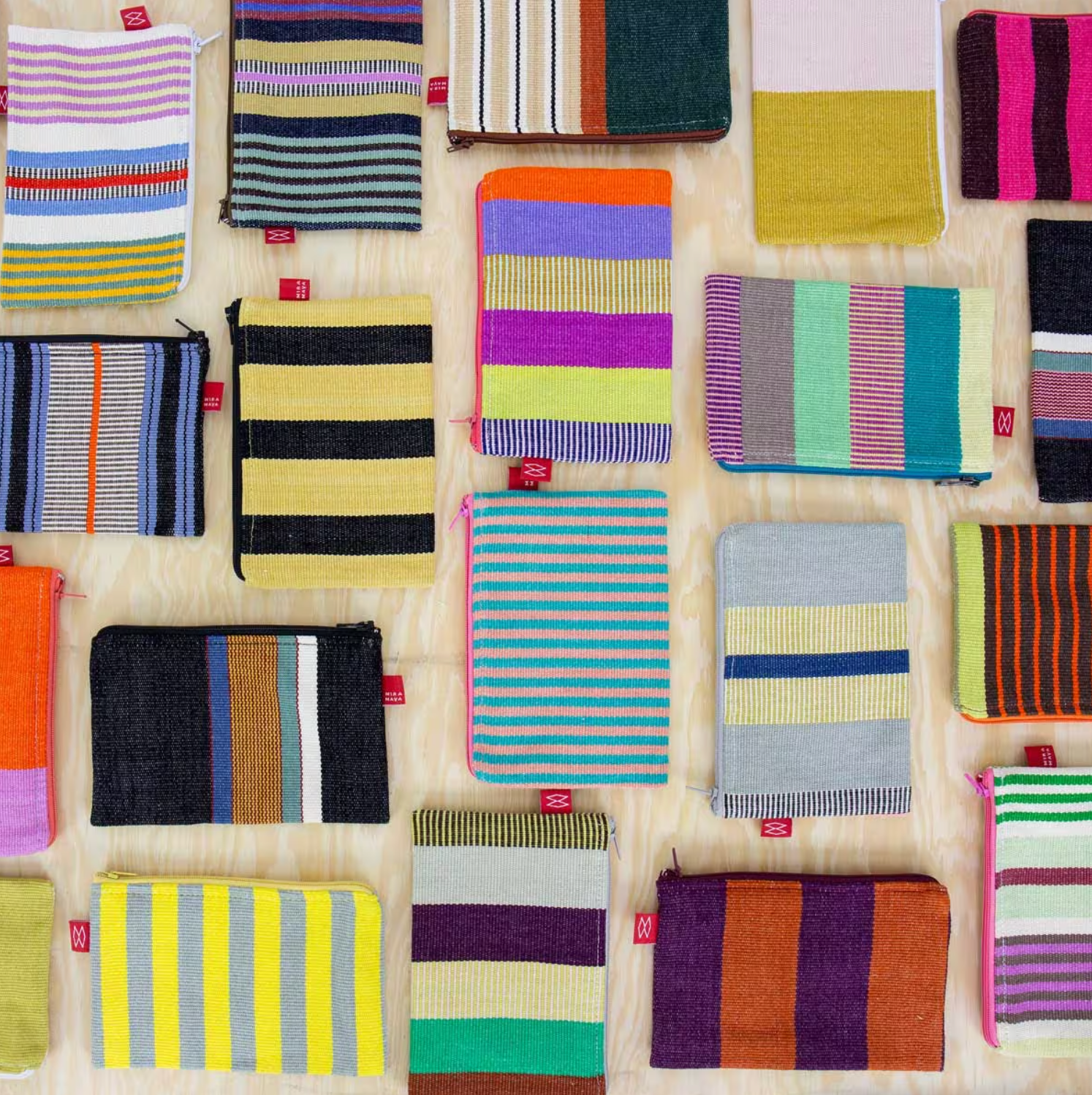 Several Mira Maya Purses by A World of Craft—handmade fair trade purses featuring colorful, striped patterns and traditional Mayan weaving—are displayed neatly on a light wooden surface.