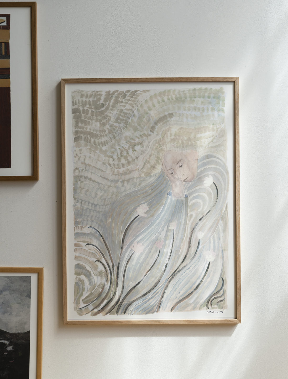 A framed abstract watercolor with swirling lines and muted tones hangs on a white wall, surrounded by other art, including the Grow Print (50x70 cm) from Fine Little Day.