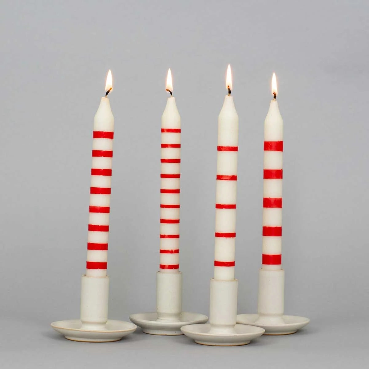 Four handcrafted soy wax striped candles in red and white from A World of Craft are displayed in white holders against a plain gray background.