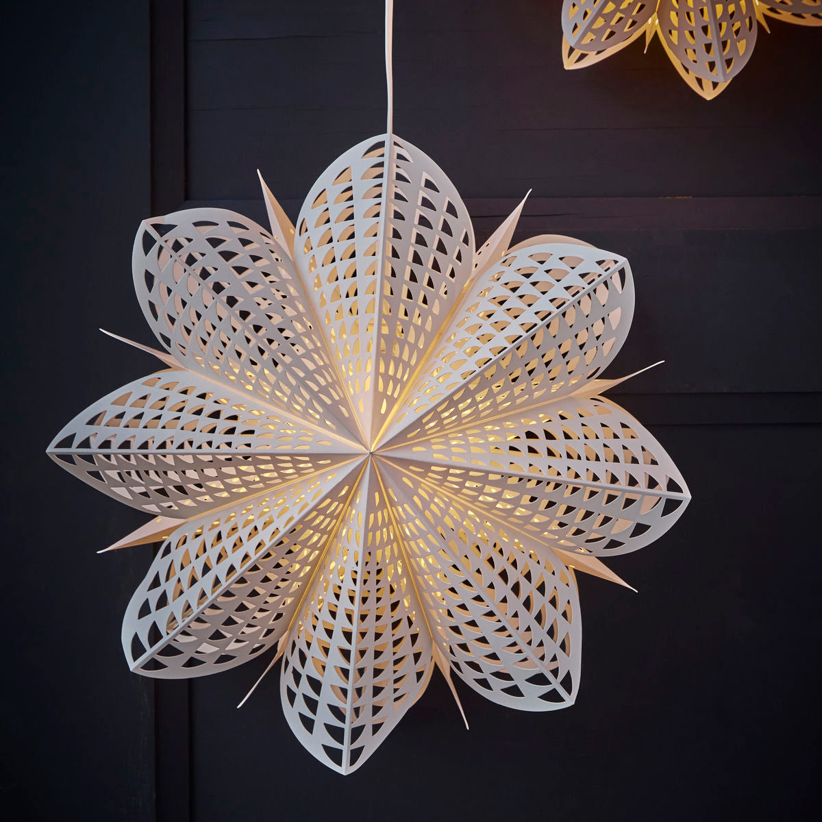The Gint Paper Star, 45 cm by House Doctor, features intricate cutouts and glows warmly, making it a stunning Christmas decoration against a dark background.