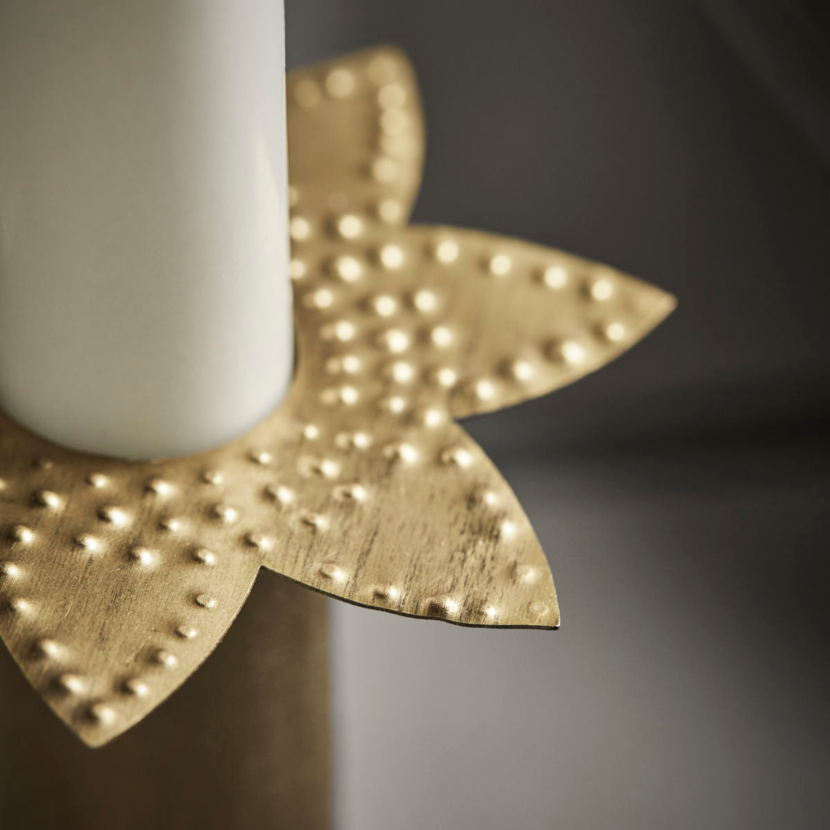 Close-up of a white candle in House Doctor's Candle Rings Star in Brass, Set of 3—gold, textured, flower-shaped holders with a matte finish—ideal for elegant Christmas decor or golden candle rings.