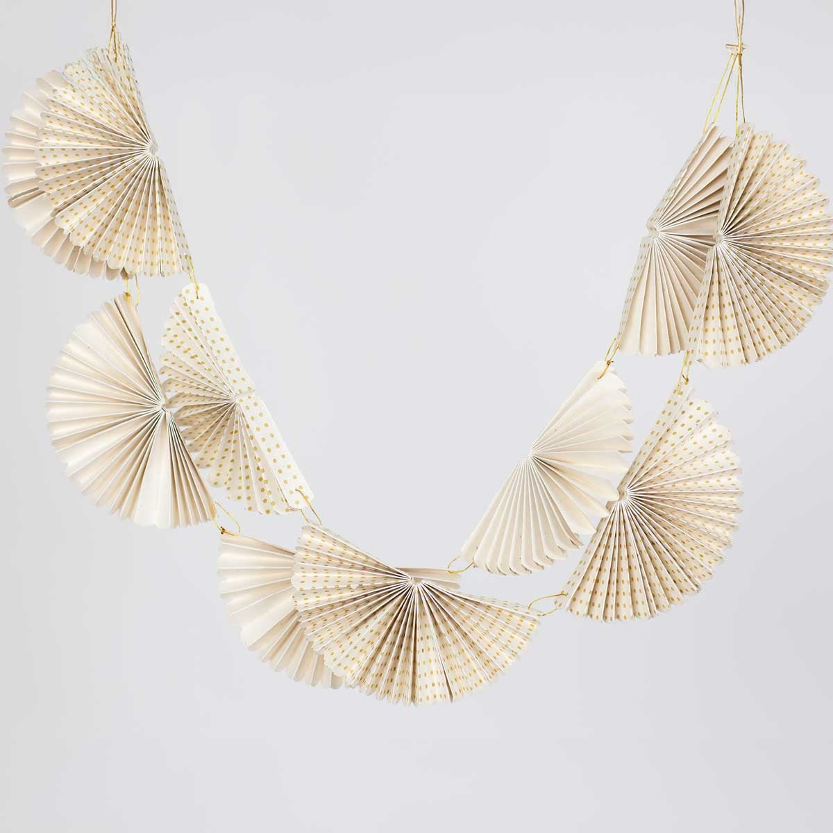 Handmade in Bangladesh, the Greta Fold Garland features six white pleated paper fans with gold polka dots strung together on a thin gold cord.