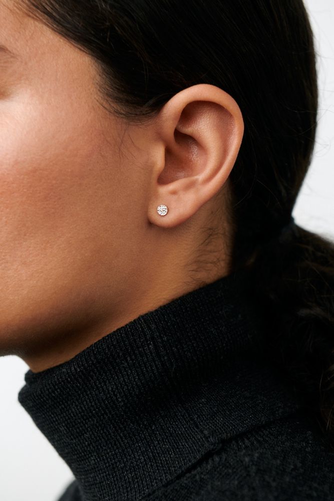 Close-up of a person in a black turtleneck wearing Pernille Corydon Mini Nature Earsticks Earrings in Silver. Their dark hair is pulled back, showcasing the simple stud design against a light background—perfect for everyday wear.