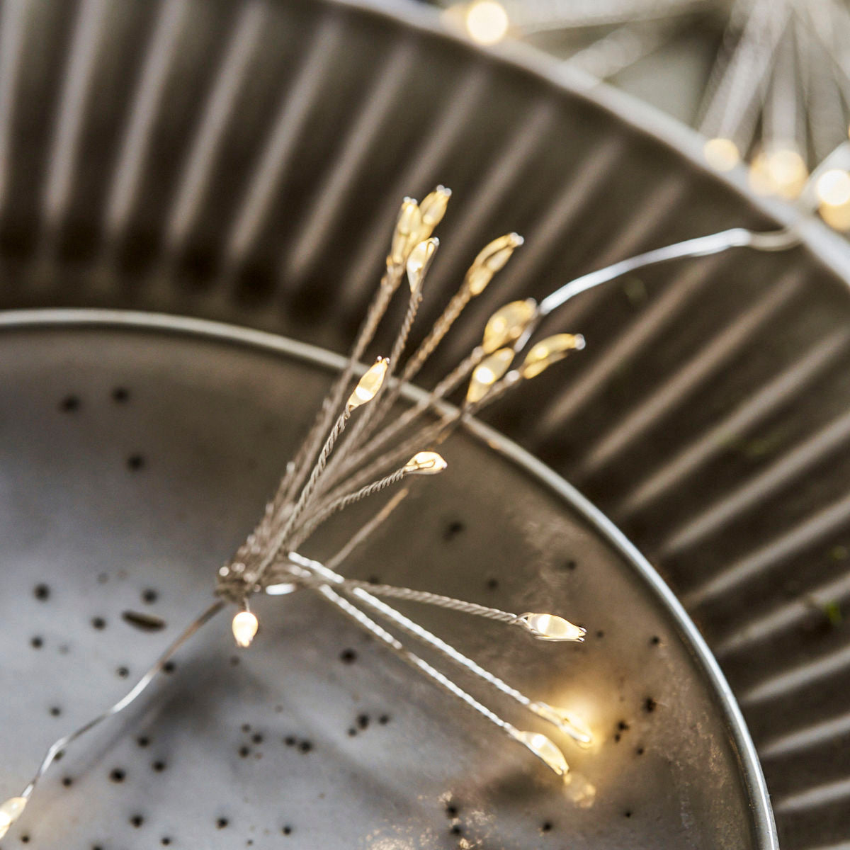 Close-up of House Doctor's String Lights, Glow LED, Silver Finish 1.5m, battery-operated and arranged in a branch-like pattern on a metal plate, glowing with a warm white light.