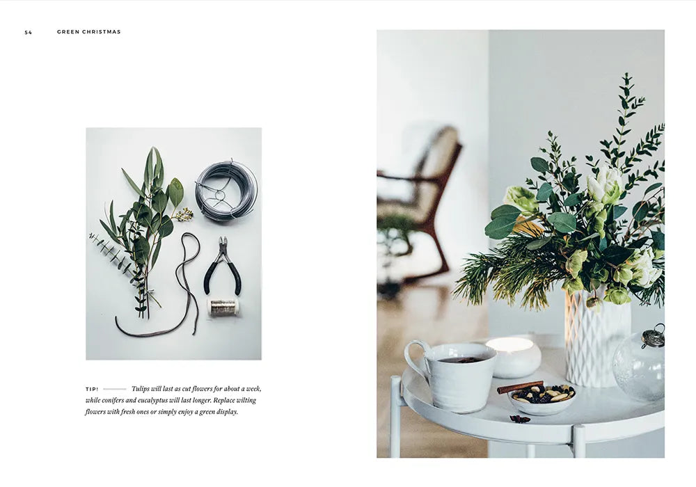 A flat lay of floristry tools and greenery, with Cozy Publishing’s Green Christmas - Wreaths & Floral Arrangements, plus a white vase, floral arrangement, teacup, and bowl on the right.