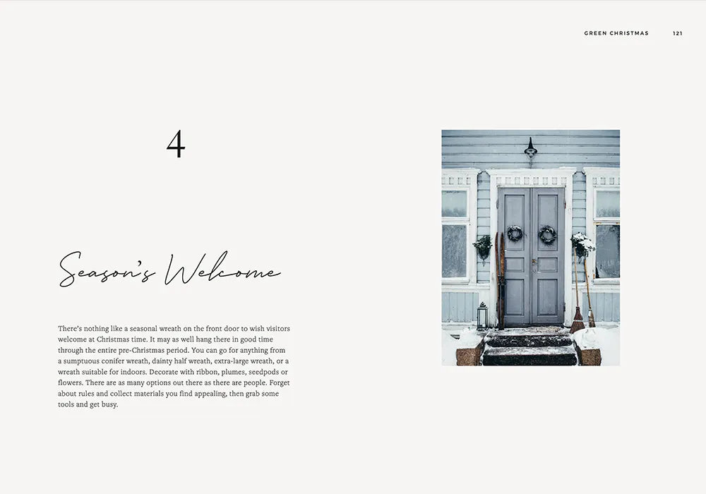 A pair of Green Christmas wreaths by Cozy Publishing adorn a light blue front door amid snowy steps and white siding, featured on a minimal magazine spread titled “Season’s Welcome.”.