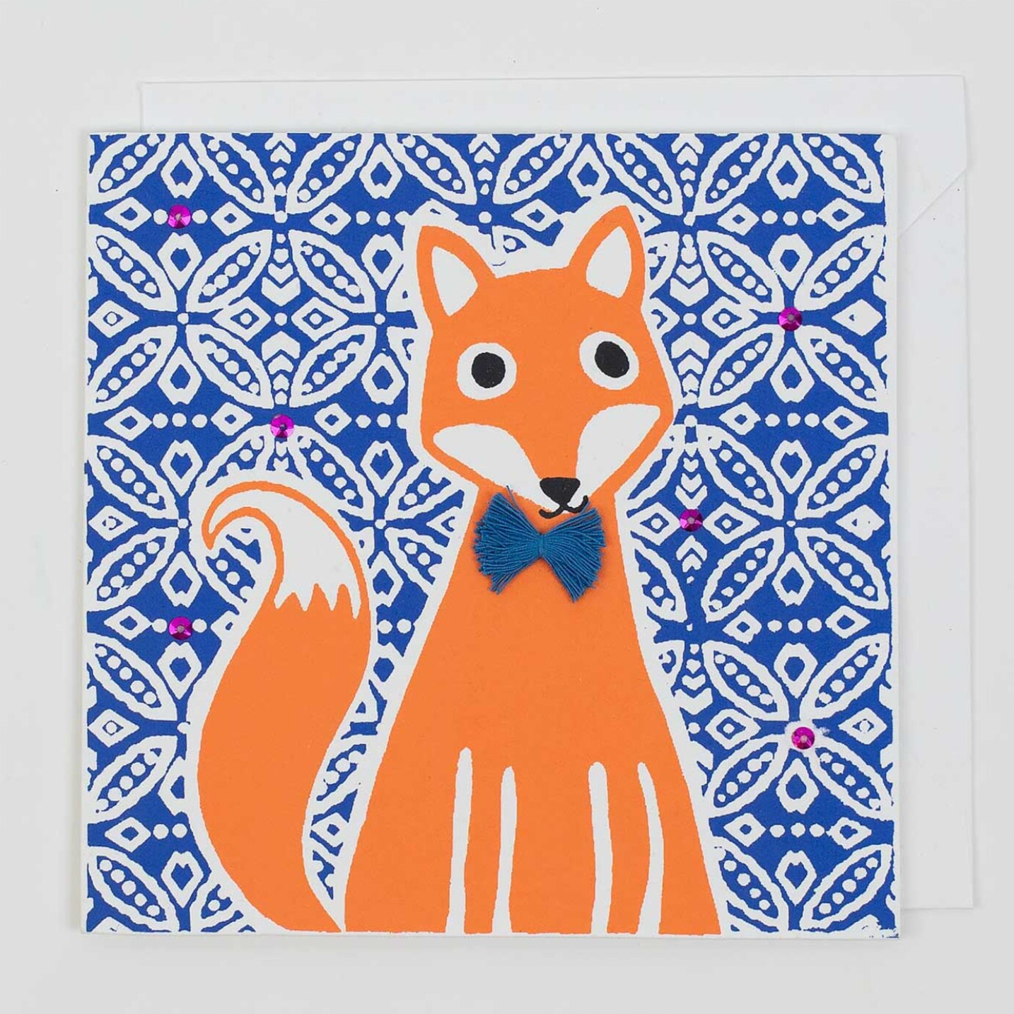 The Fox Handmade Greeting Card by A World of Craft features an orange fox with a white-tipped tail and blue bow tie, sitting before a blue and white patterned background with pink accents—a charming, fair trade card for any occasion.