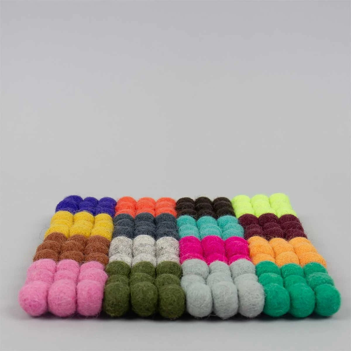 Rows of colorful felt balls are neatly arranged in a rectangular grid, forming the Natural Wool Pot Holder by A World of Craft—a vibrant, fair-trade kitchen accessory handmade from natural wool.