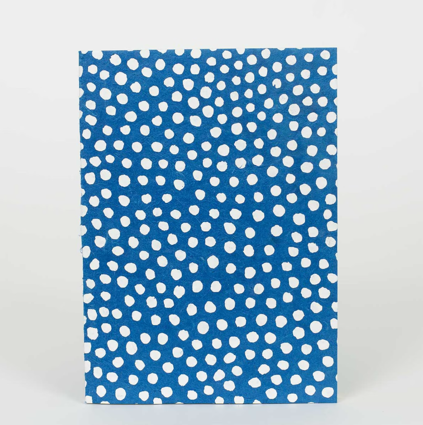 The A World of Craft Dotted Notebook, Blue, A5, features an irregular white polka dot pattern on its eco-friendly cover and is shown standing upright against a plain white background.