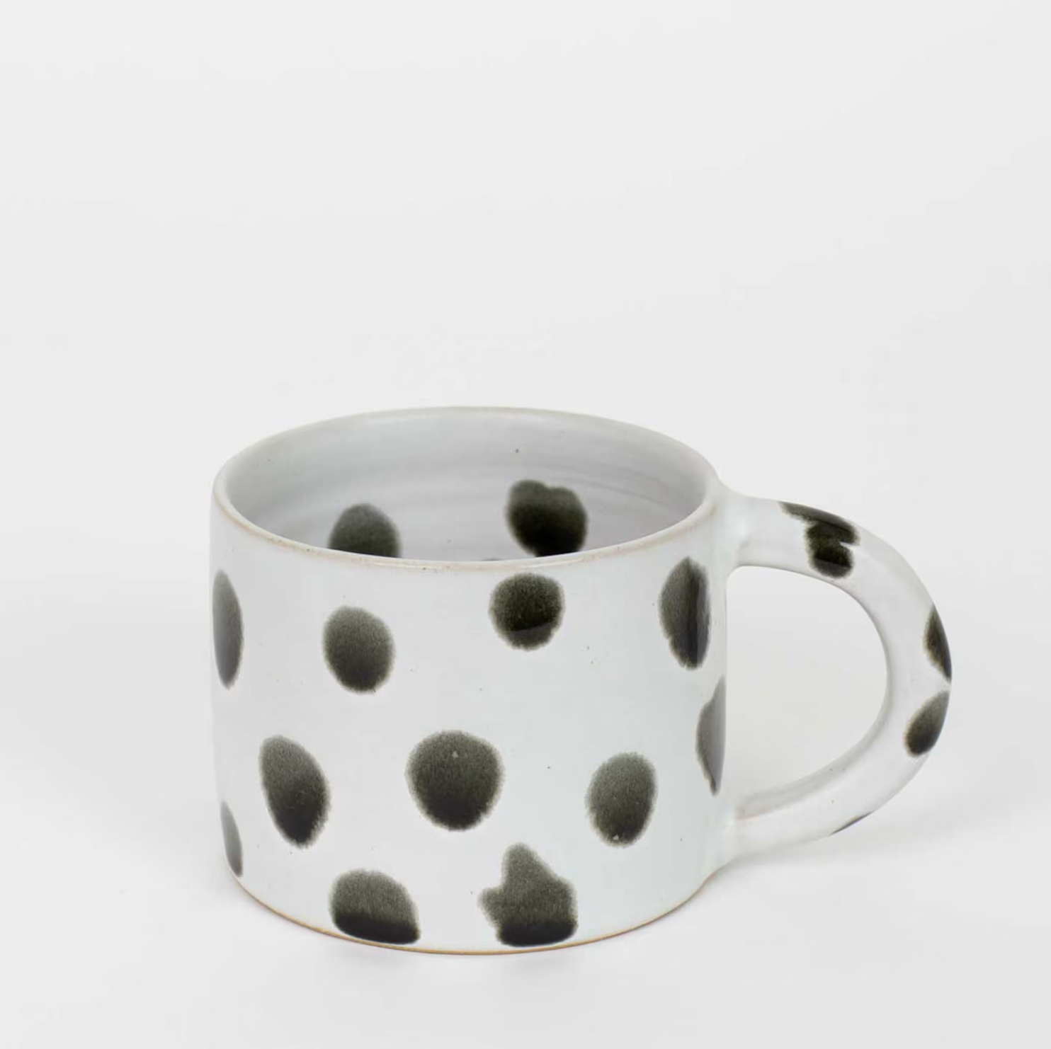 The Blot Coffee Mug by A World of Craft features a handcrafted white ceramic design with irregular black and grey polka dots, including on the handle, shown against a plain white background.