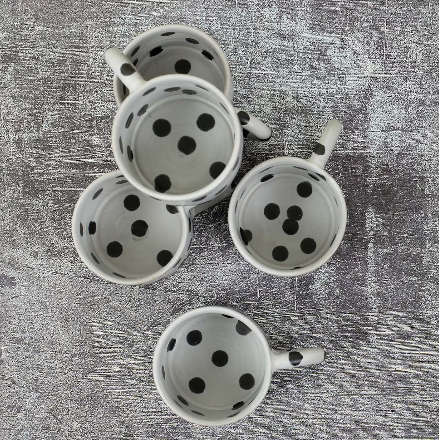 Five Blot Coffee Mugs by A World of Craft, featuring black and grey designs, are arranged on a textured gray surface and viewed from above.