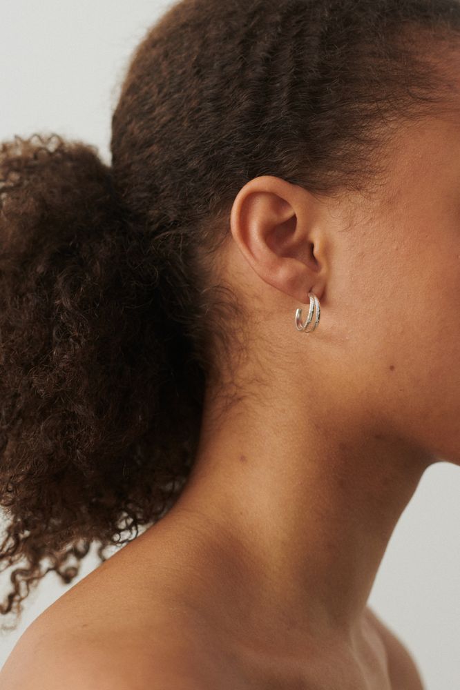 A close-up of a person with curly hair wearing Pernille Corydons Poetry Hoops in Silver in their left ear.
