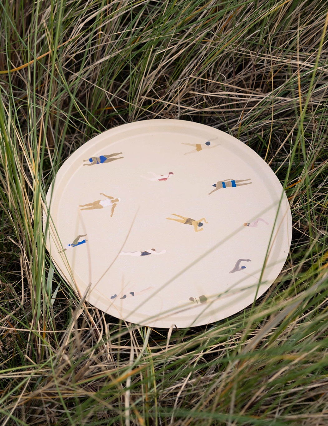 Round birch wood tray featuring colorful swimmer illustrations, set against a natural grassy background.