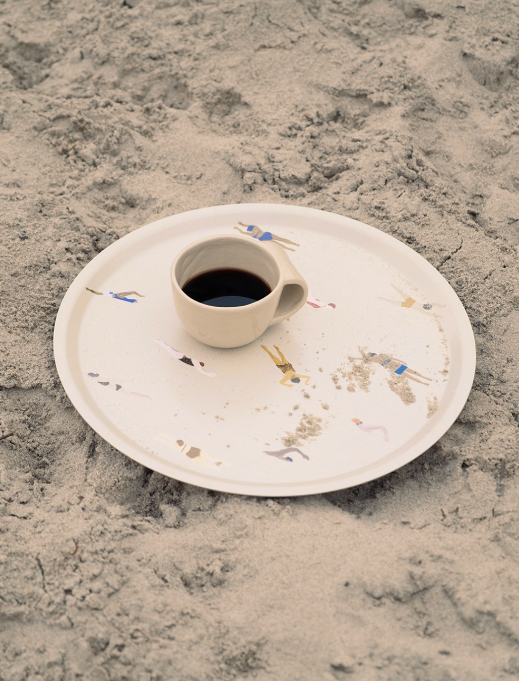Round birch wood tray with Swimmers print, holding a cup of coffee on sandy surface, perfect for serving in style.