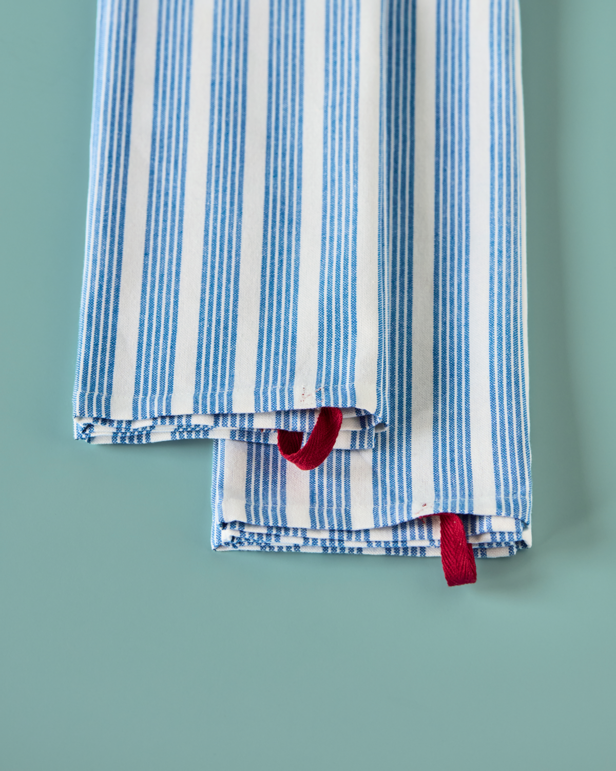 The House Doctor Tea Towels Chef, Set of 2 in Blue & White, feature neatly folded cotton towels with blue stripes and red hanging loops, displayed on a light blue surface.