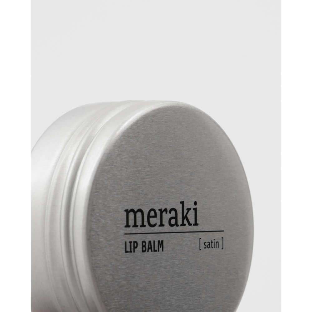A close-up of a round, silver tin of Meraki Organic Lip Balm, Satin, with organic natural oils, set against a plain white background.