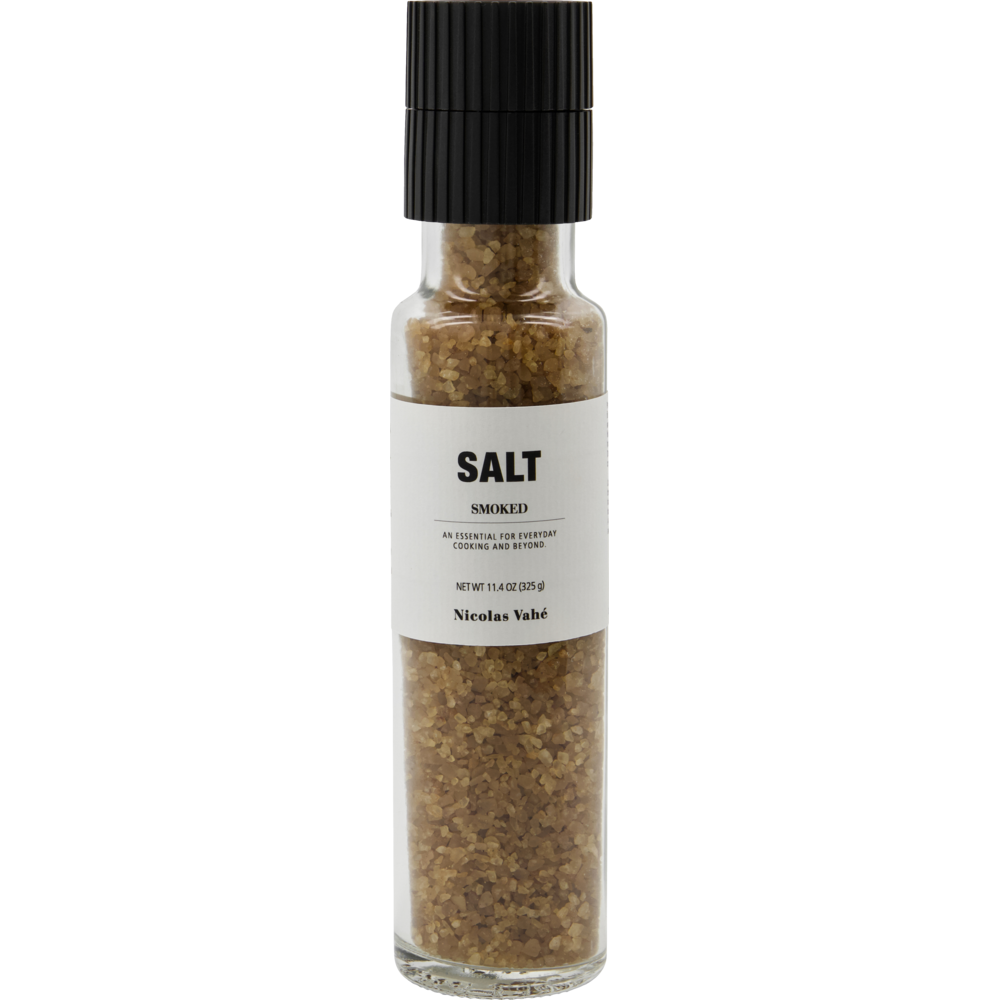 A clear glass grinder bottle filled with brown beechwood-smoked salt crystals. The label reads "Salt, Smoked" with additional text below and "Nicolas Vahé" at the bottom. Finished with a black grinder top.