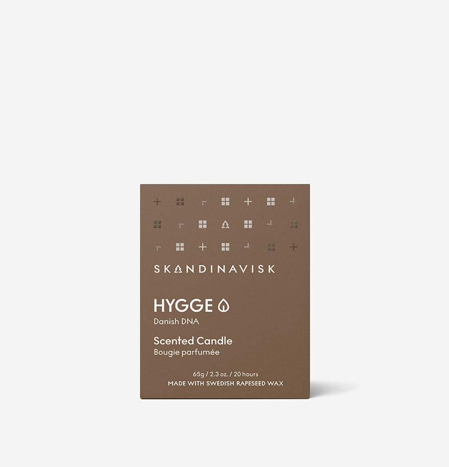 A brown box labeled Skandinavisk Mini Scented Candle Hygge 20h, 65g, crafted from Swedish rapeseed wax, with minimalist icons and white text.