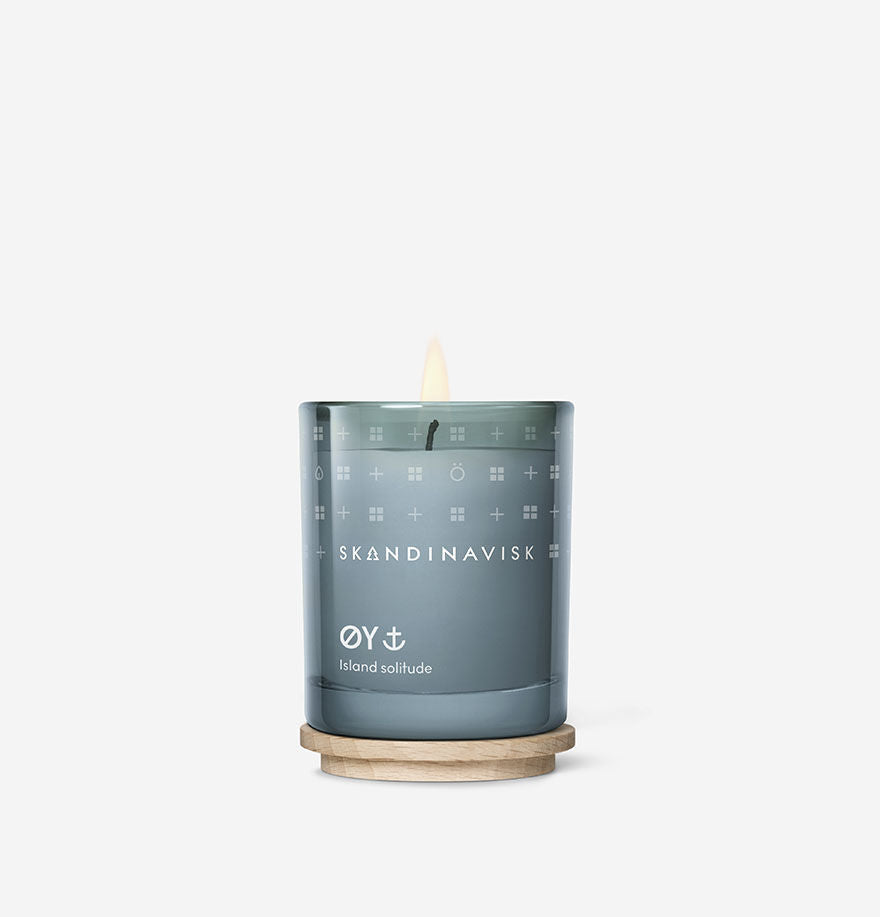 A lit Skandinavisk Mini Scented Candle Oy 20h, 65g, crafted from Swedish rapeseed wax, sits on a round wooden base against a plain white background.