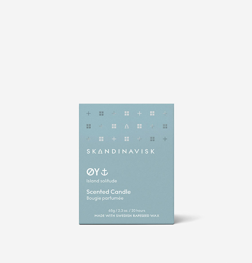 A blue box of Skandinavisk Mini Scented Candle Oy 20h, 65g features white text, minimalist icons, an engraved beechwood lid, and notes Swedish rapeseed wax at the bottom.