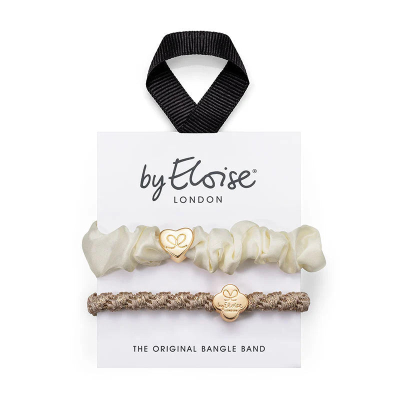 Set of two hairbands from ByEloise: one cream, ruffled like a silk scrunchie and finished with a gold heart charm, and one taupe bangle band featuring an elegant braid and a gold round charm. Presented on a branded card with a black ribbon loop at the top, the Bangle Band Cream & Gold Set by ByEloise makes for perfect hair accessories for any occasion.